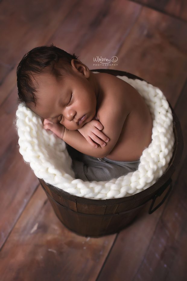 Newborn in a bucket on wood backdrop