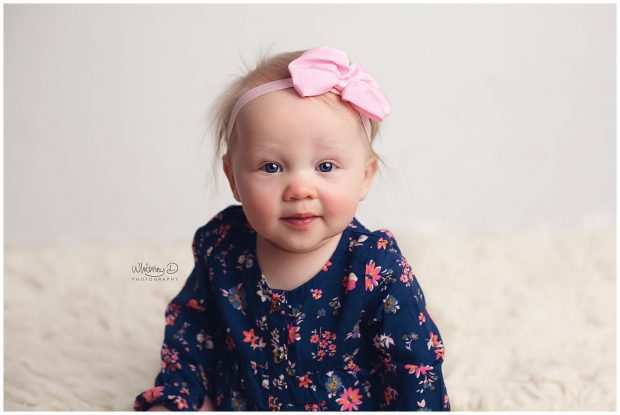 Six month old baby on white backdrop wearing a pink bow at Whitney D. Photography in Conway, Arkansas