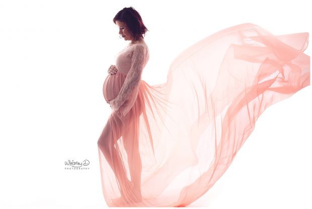 Pregnant mom in pink and peach maternity gown on white backdrop at Whitney D. Photography in Conway, Arkansas